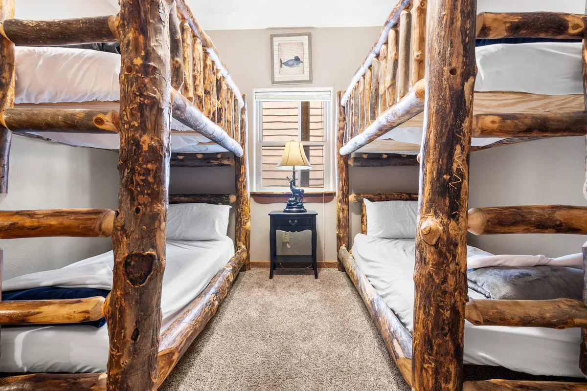 A playful and family-friendly bunk room with multiple bunk beds, a table lamp, a mirror, and whimsical framed fish-themed art. The space is bright and inviting, designed for kids and teens to relax, play, and bond after busy days.