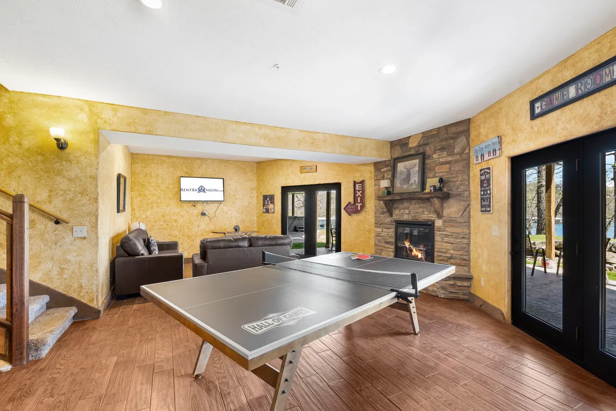 The image captures a lively rec room featuring a ping pong table, a cozy sofa, a flat-screen television, and a stone fireplace. The space is well-lit, inviting, and designed for relaxation, friendly competition, and movie nights.