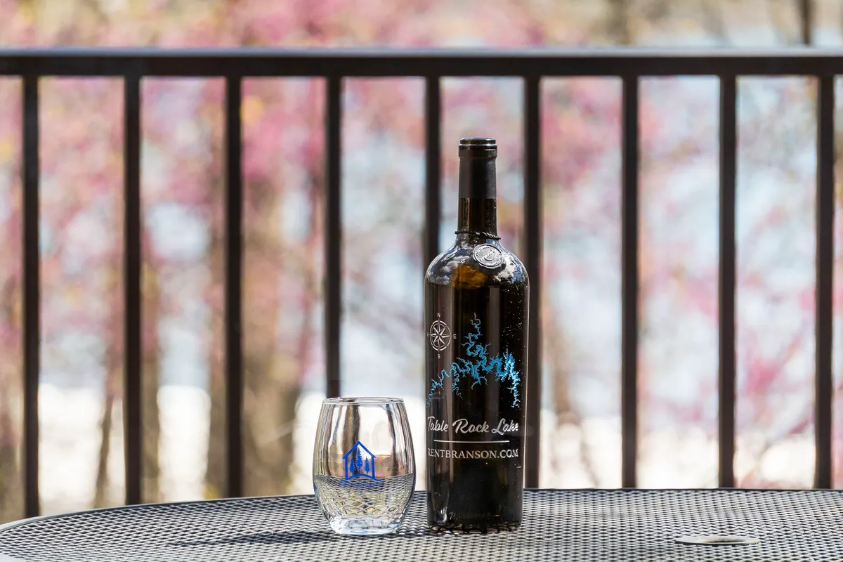 A close-up, tranquil outdoor setting featuring a wine bottle and glass set against the backdrop of nature, evoking a sense of relaxation on a balcony or deck. The image suggests enjoying local wines while unwinding and taking in the views—perfect for adults looking for a serene moment with friends.