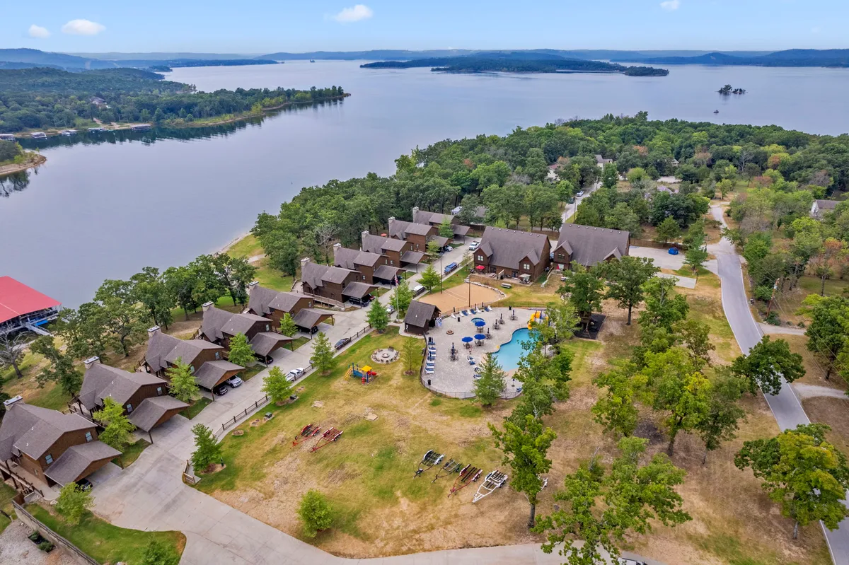 A vibrant exterior shot showcasing multiple resort amenities: the lake, a swimming pool, several inviting cabins, a playground, and surrounding trees. The scene is bustling with opportunities for swimming, boating, hiking, and gathering outdoors, presenting a joyful, active mood perfect for group retreats.