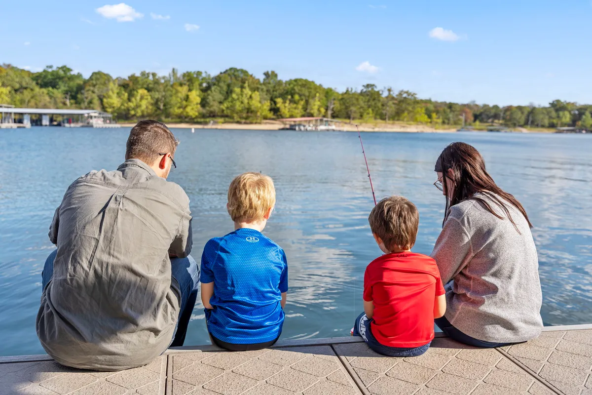 A joyful family scene at the lake's edge, with children and adults fishing together. The setting is vibrant and natural, highlighting direct access to the water, family bonding, and the classic lakeside activities referenced in the section.